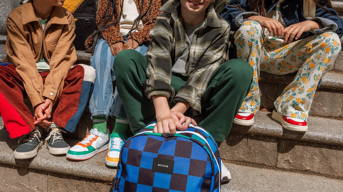 Kids sitting on school steps with a blue checkered STATE Bags Kane backpack