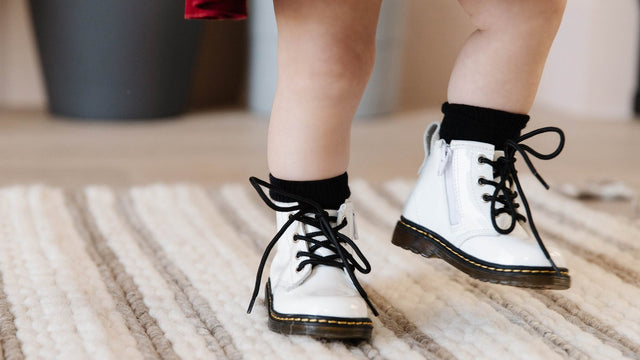 Toddler standing on a striped rug in white lace-up boots with long black laces