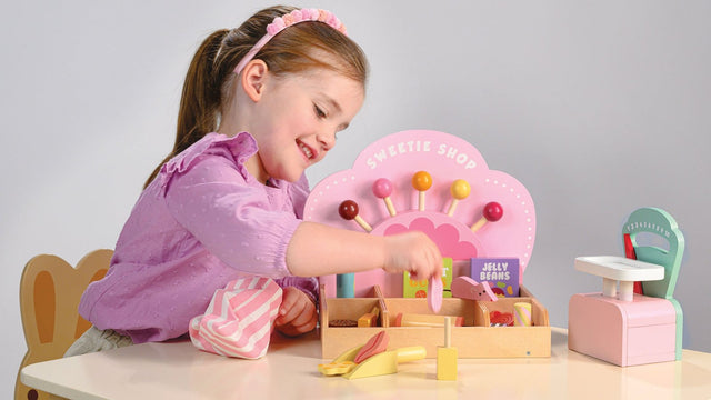 Girl playing shopkeeper at a wooden sweetie shop pretend-play set with a toy cash register