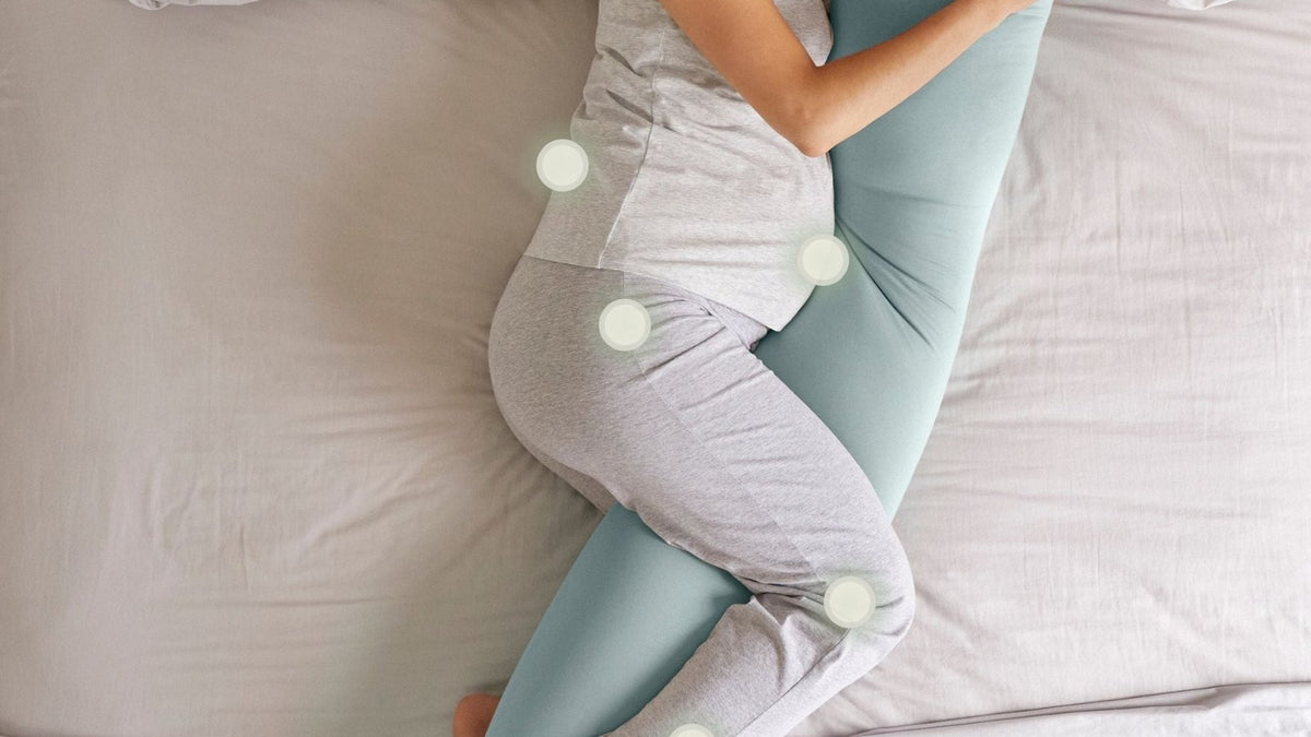 Pregnant woman resting on her side in bed with a full-length pregnancy pillow