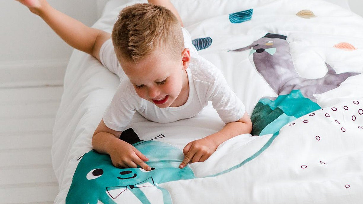 Happy toddler playing on his new big-kid bed with a jellyfish toddler comforter - toddler bed transition and bedding guide