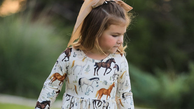 Toddler in a long-sleeve horse-print twirl dress playing on the lawn — best toddler dresses guide