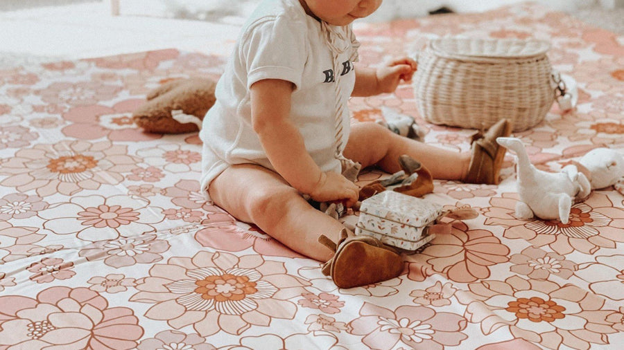 Baby sitting on a Toki Mats Blooms organic cotton play mat with toys