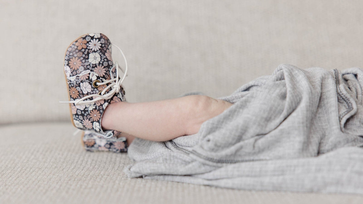 Baby's foot in a floral soft-sole lace-up crib shoe resting on a sofa