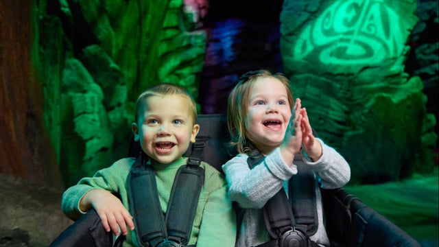 Two laughing toddlers riding harnessed in a WonderFold stroller wagon