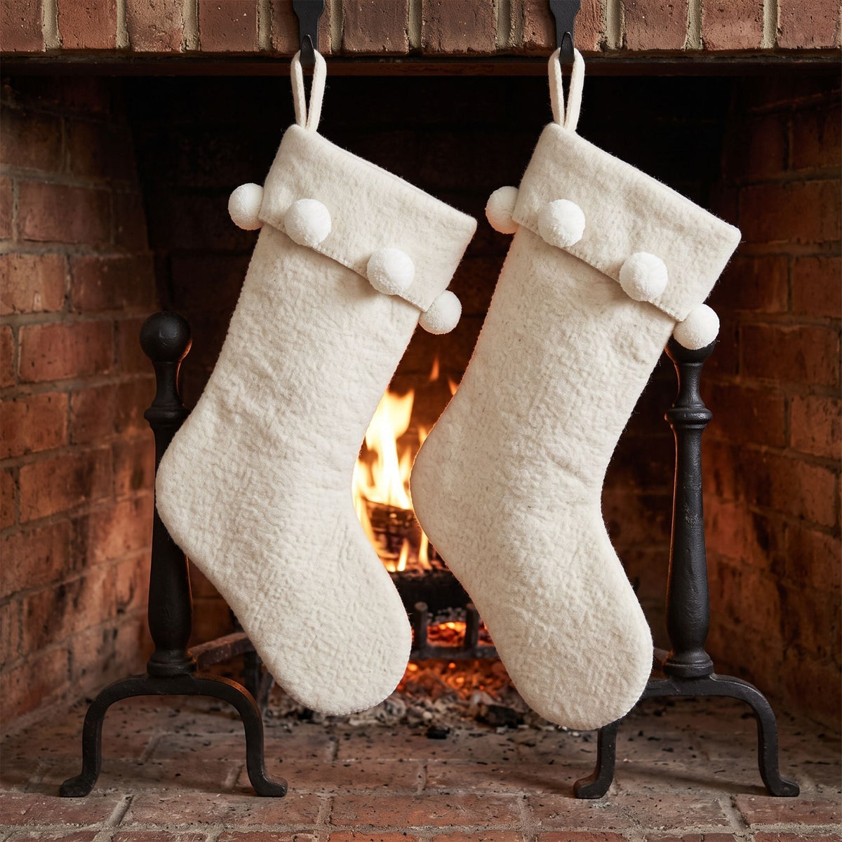 Two cream pom pom wool Christmas stockings hanging by a fireplace