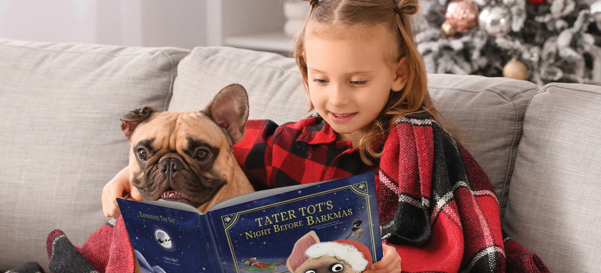 Girl in plaid pajamas reading a Christmas book with her dog